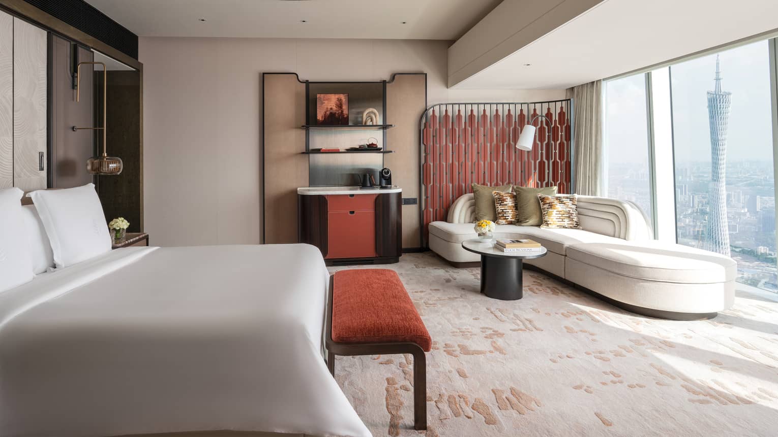 Sleek hotel room with king bed, sofa, wet bar and wall of windows with view of iconic city tower