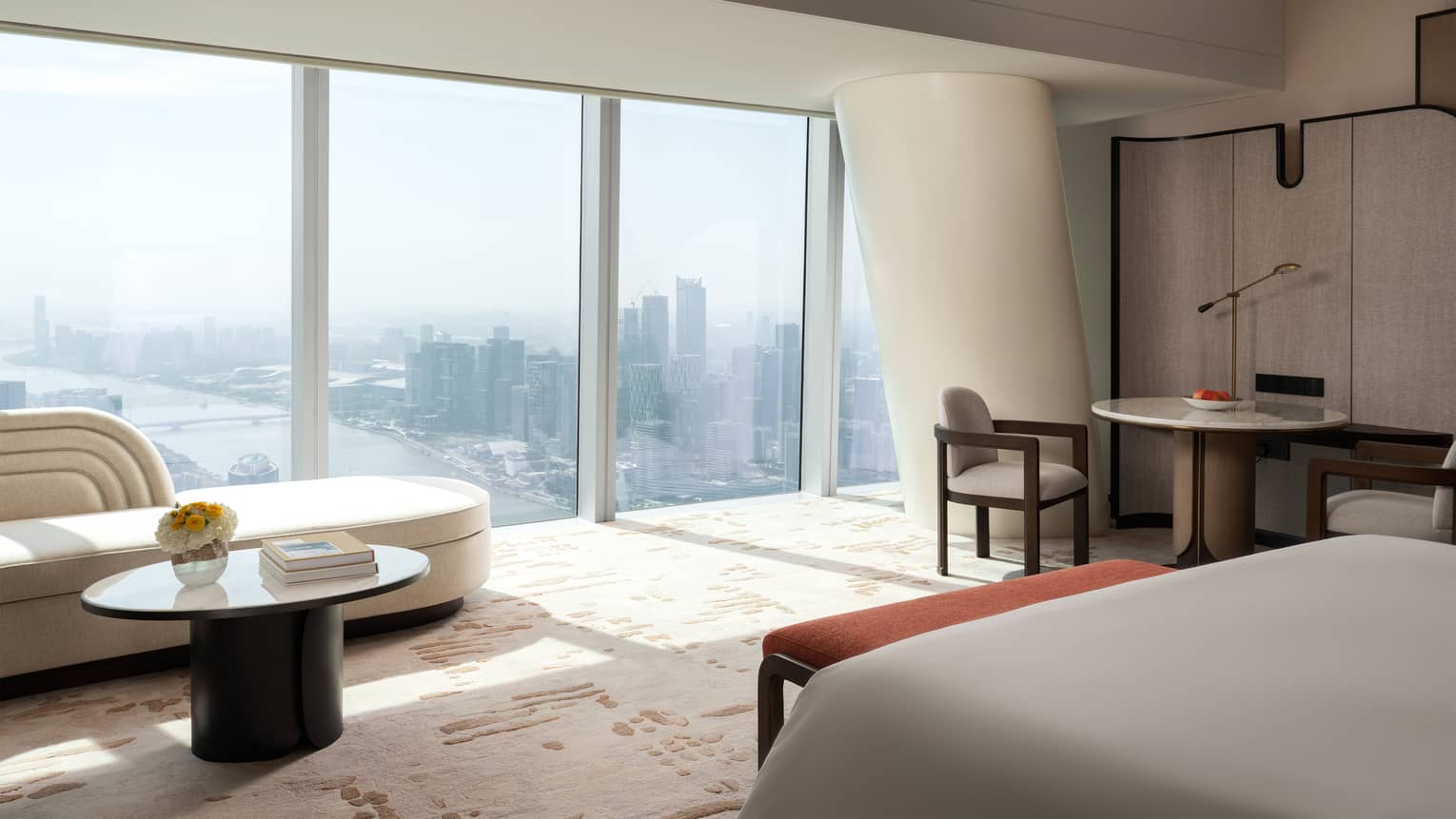 Sleek hotel room featuring king bed, chaise and wall of windows with city view