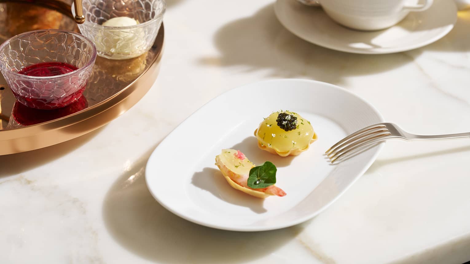 Two colourful pastries on a white plate, with a cup of hot tea in the background
