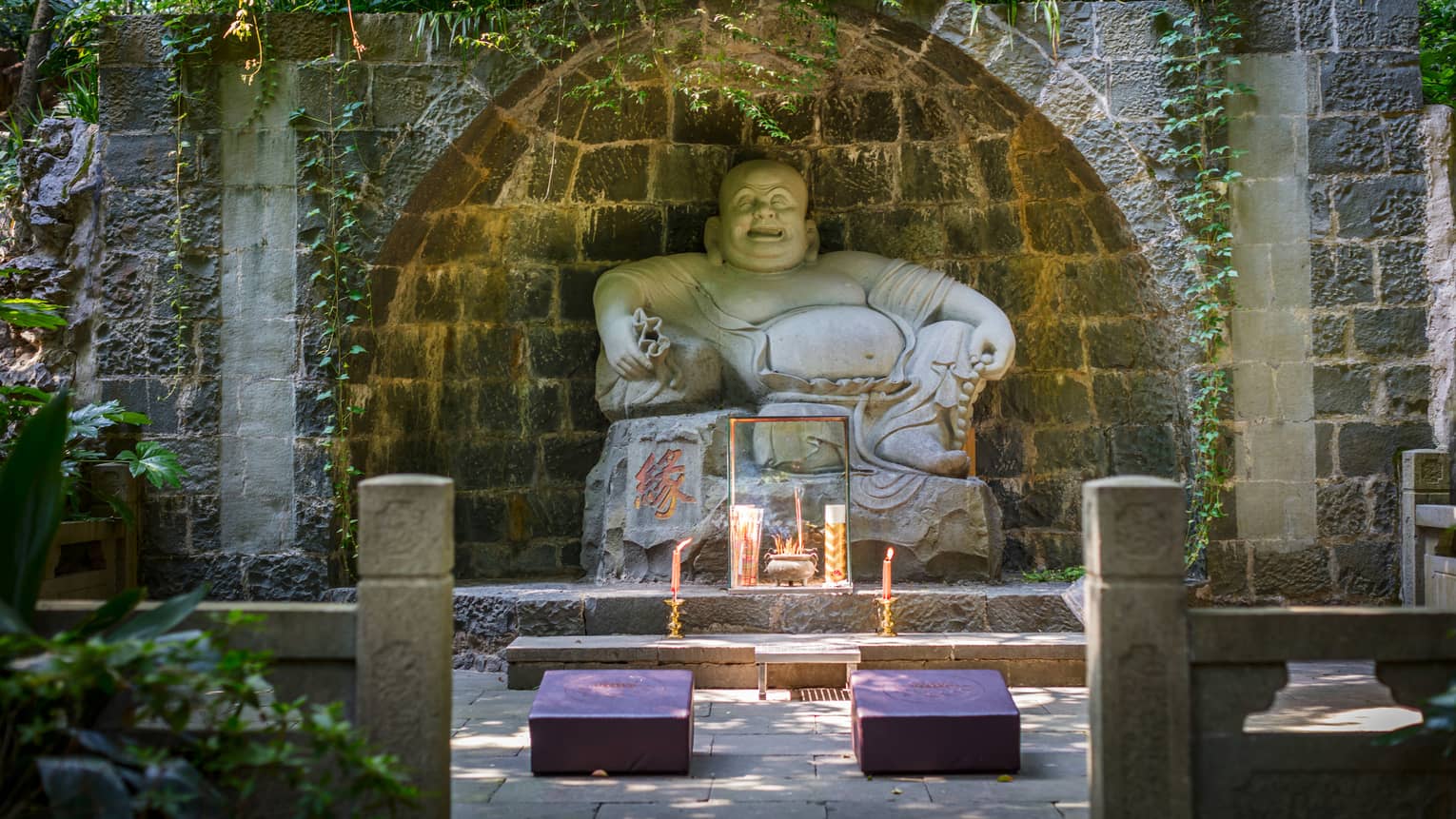 Large Buddha statue in front of altar, candles in temple garden