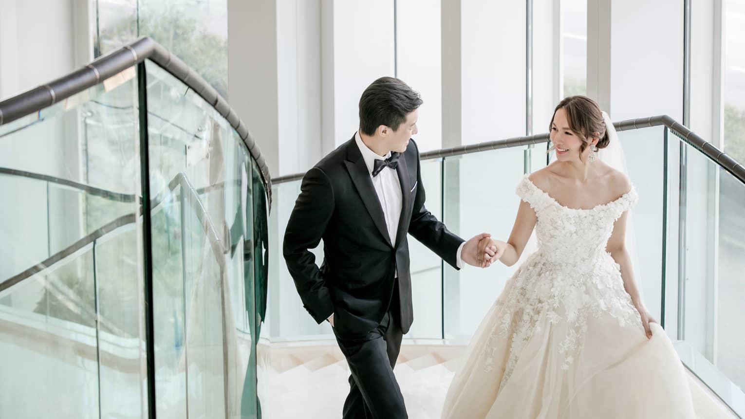 Bride and groom walk up a glass staircase
