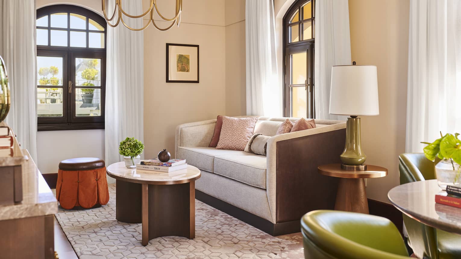 Living room with light pink walls, grey sofa, two arched windows, chandelier, coffee table