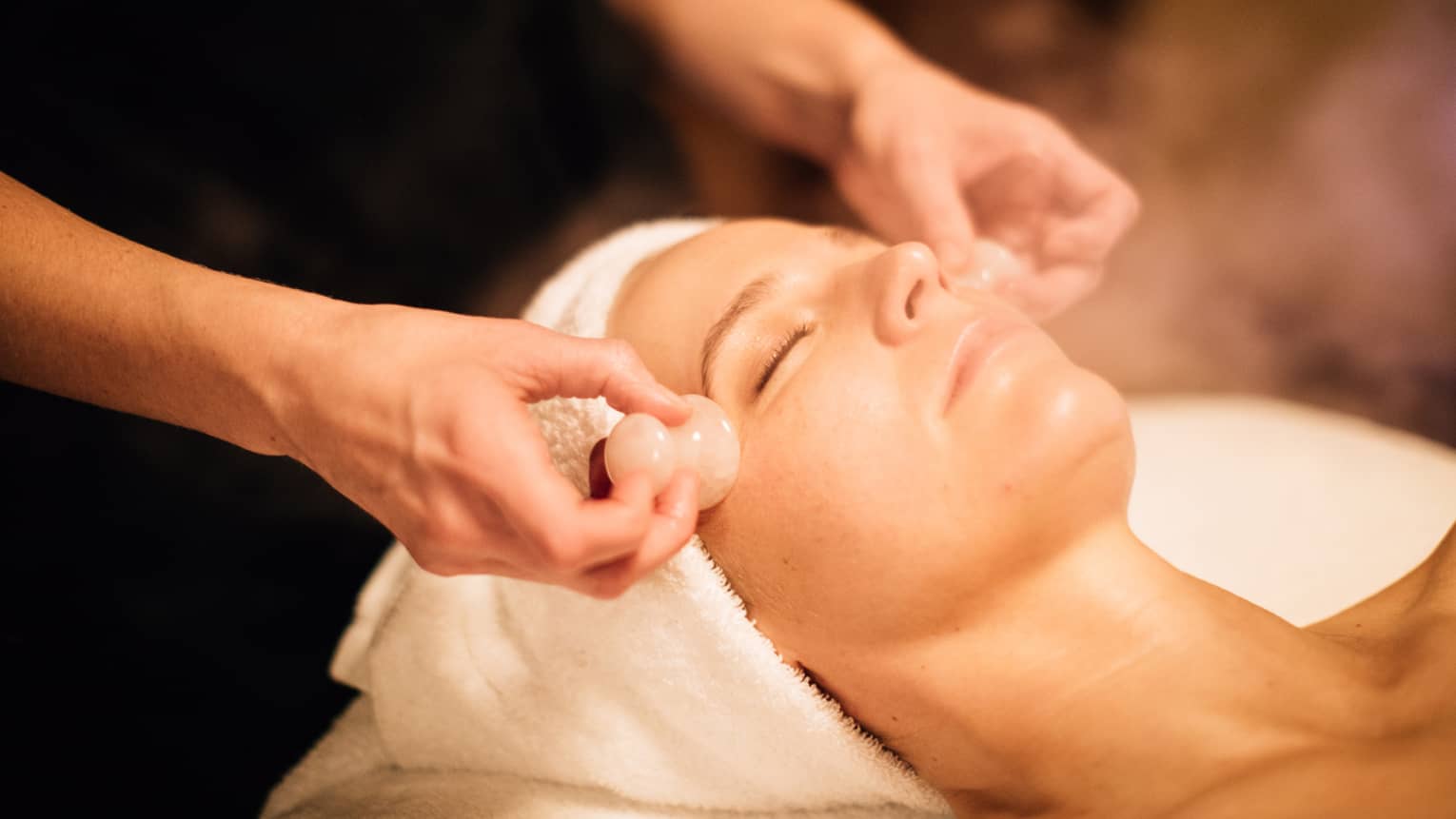 A woman receiving a facial massage with round stones.