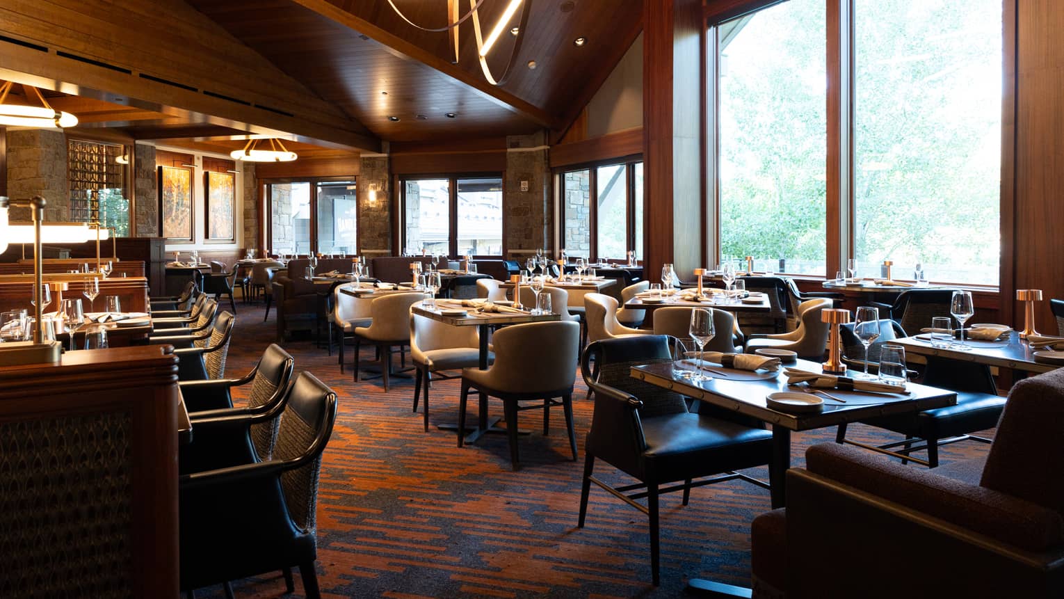 A restaurant with tables set with glasses and silverware, and windows along the sides of the room