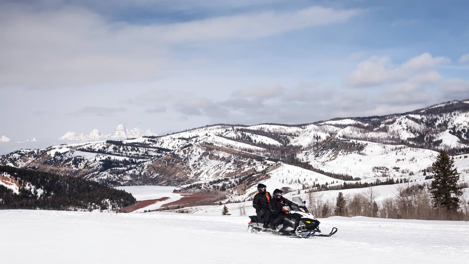 Aerial view of two people riding on a snowmobile in front of snowy mountains