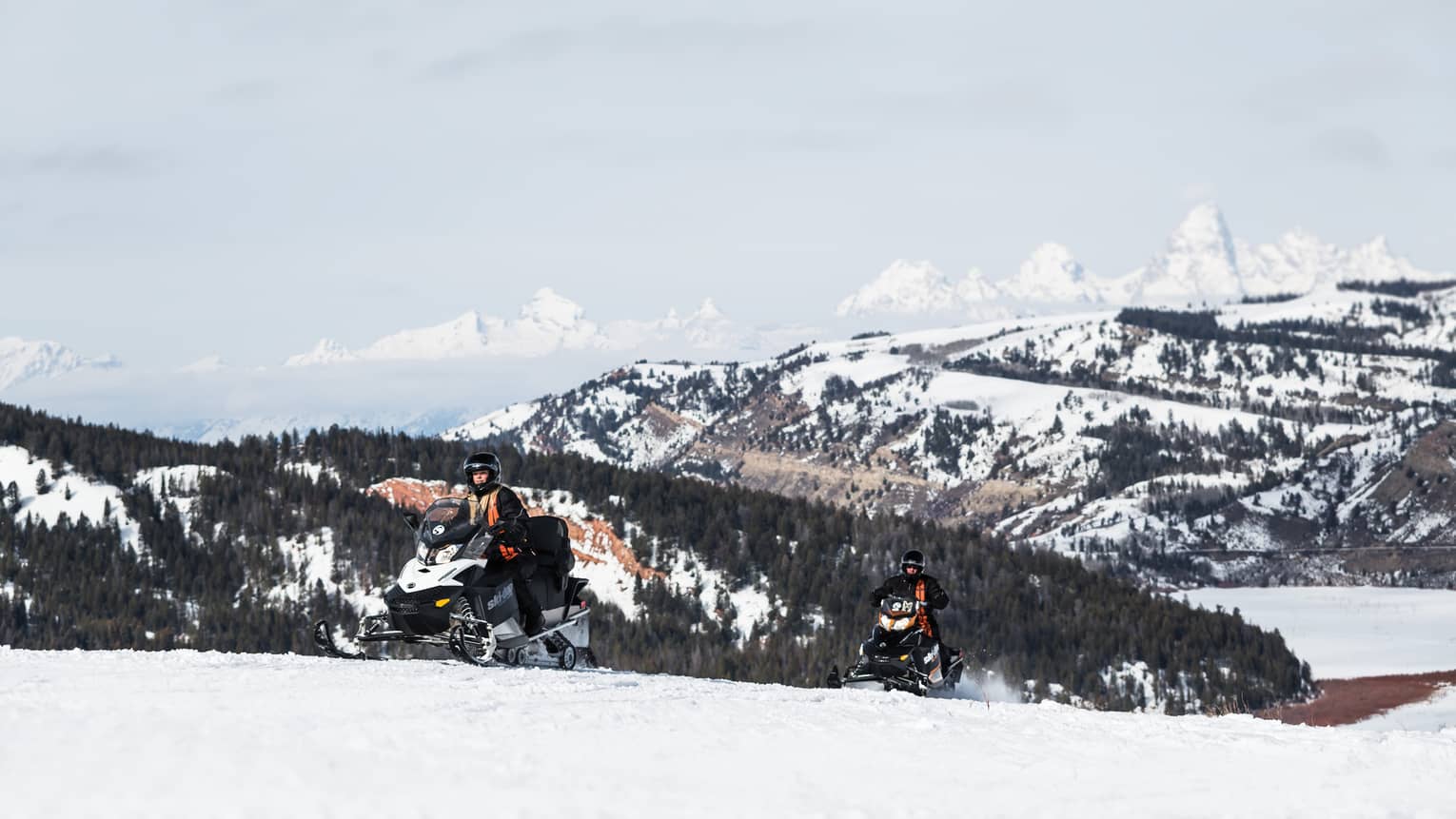 Person in snow gear on snowmobile with snowy mountain in backdrop