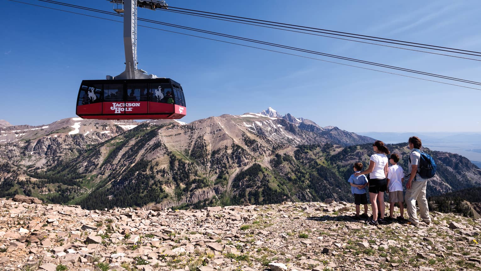 A family of four watches from a cliff as a ski lift passes by