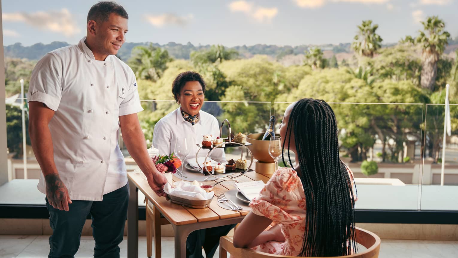 A chef visits a table where two women sit enjoying afternoon tea, with garden view