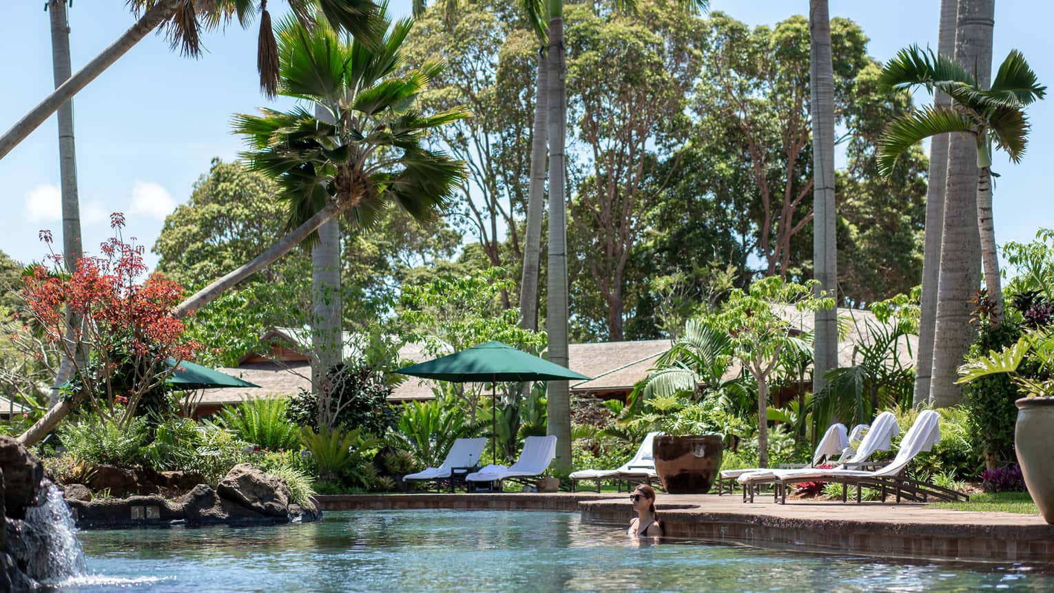 Female guests relaxes in the outdoor pool surrounded by palm trees