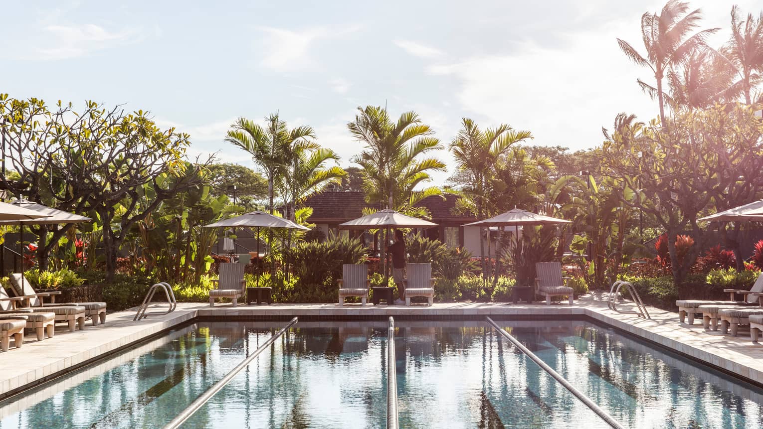 Lap pool at Four Seasons Resort Hualalai with lounge chairs in the shade of umbrellas and palm trees in the wind