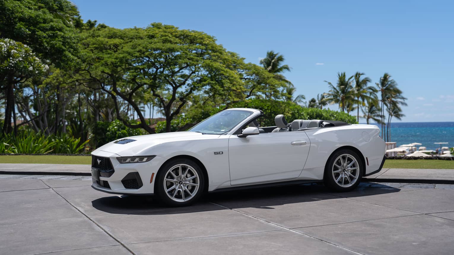 White convertible car parked in front of tropical beach setting