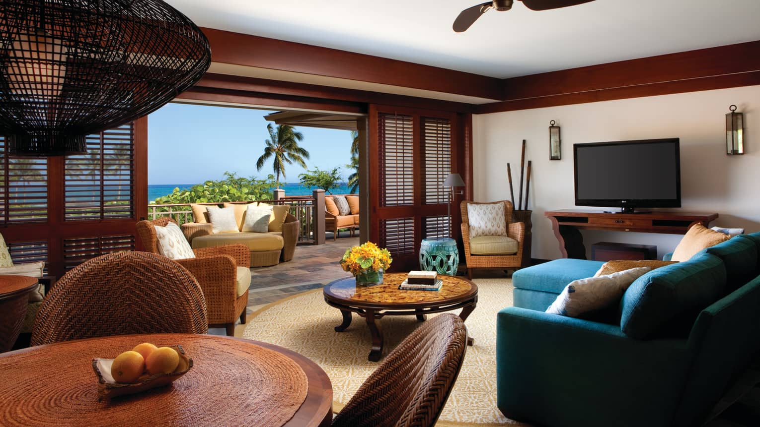 Deluxe Suite living room with blue sofa, round wood dining table, open wood shutters to large patio