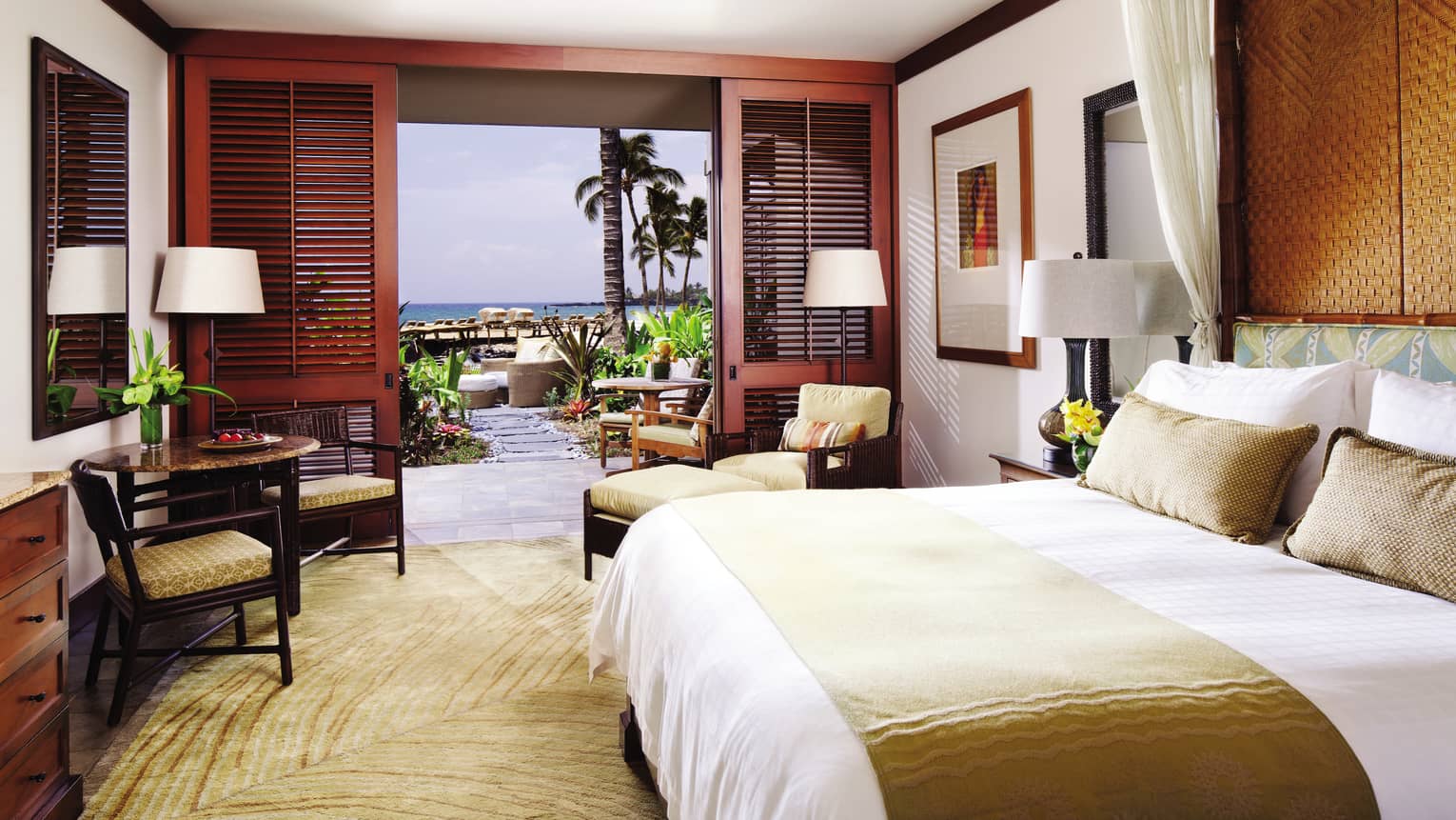 Ocean-View Deluxe Room bed with gold silk sash, pillows, gold chairs by wood patio shutters