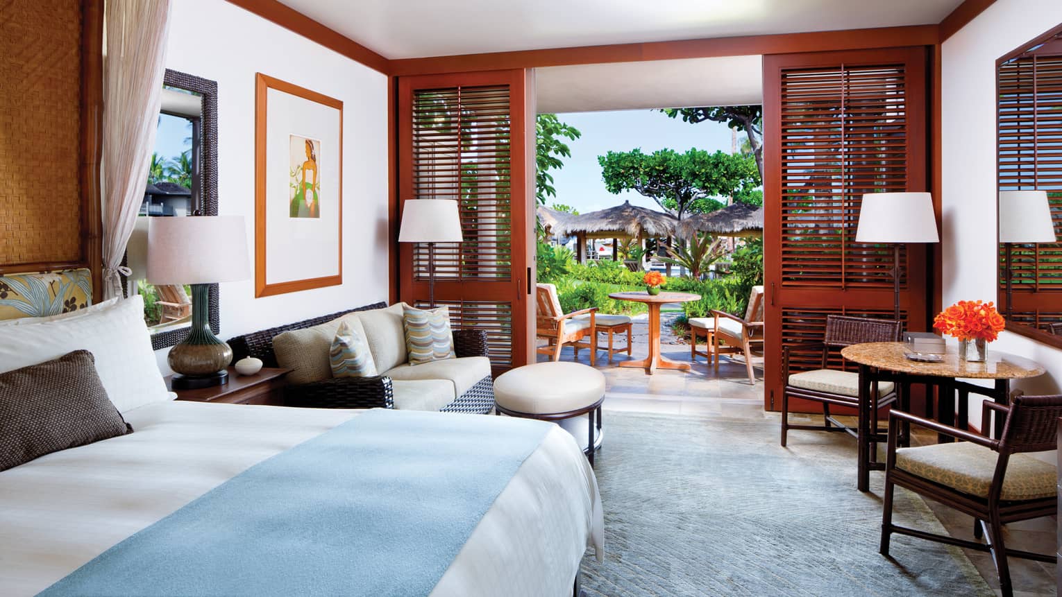 Poolside Room bed with blue blanket, wicker loveseat and ottoman, table, open wood patio shutters
