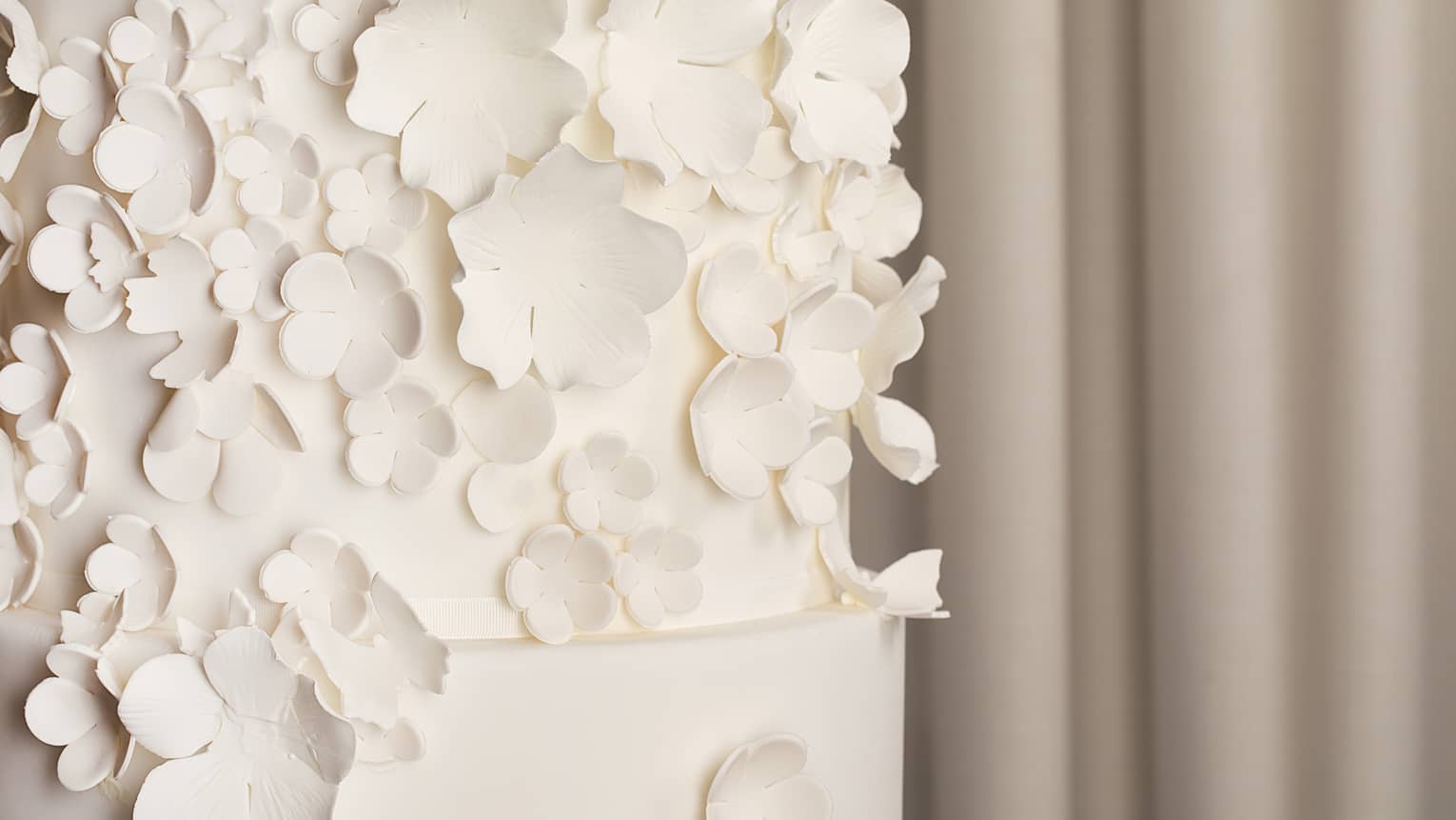 Close-up of a three-tiered white wedding cake with white fondant flowers placed going up one side