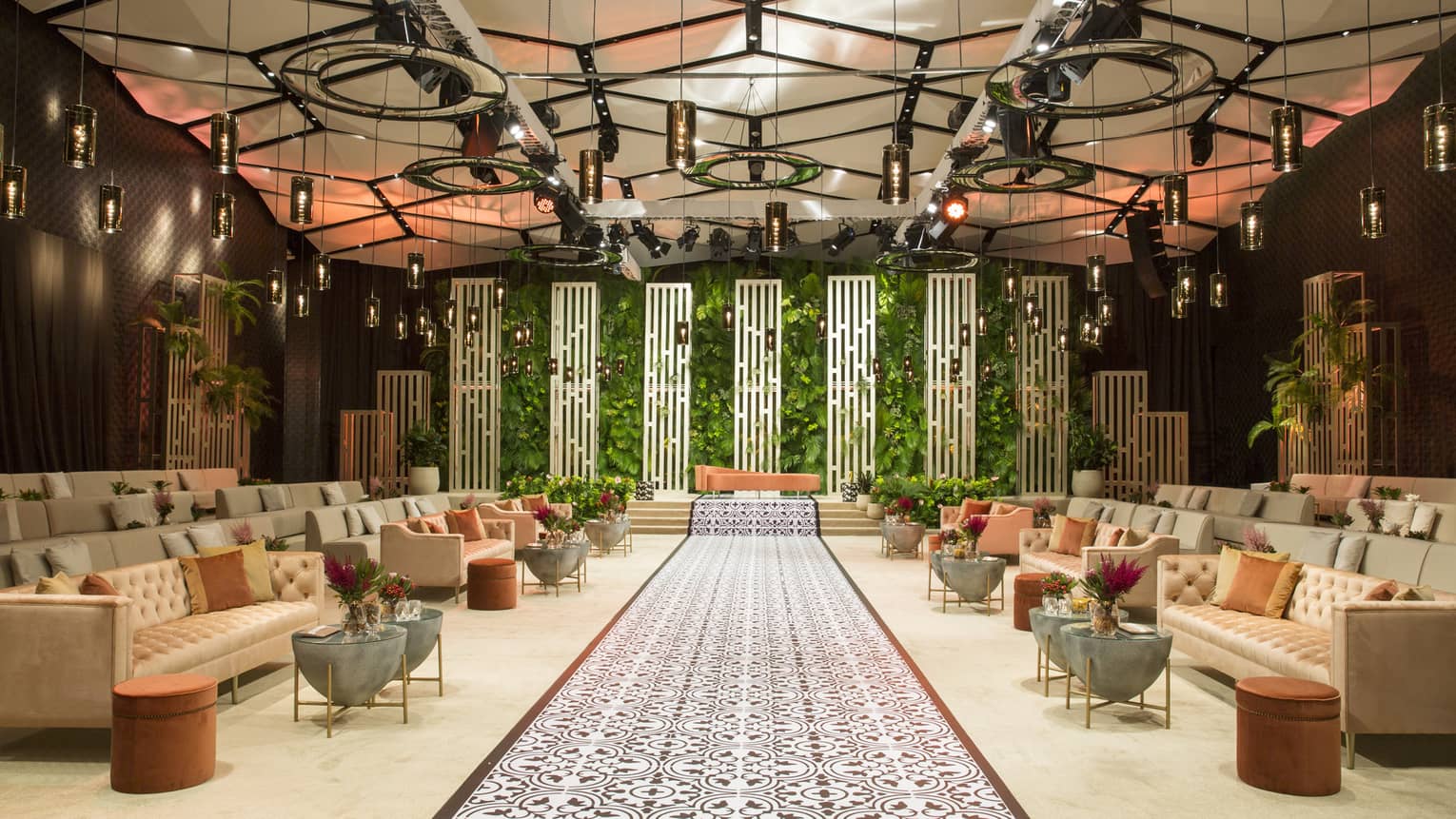 Rows of sofas line aisle towards stage with living wall, planters in ballroom with geometric ceiling