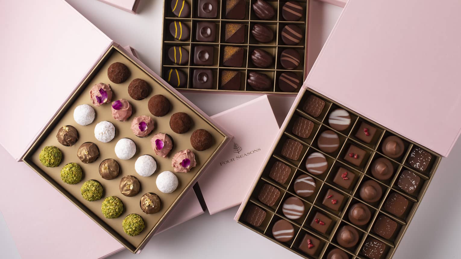 Three square pink boxes open to reveal 25 chocolate truffles within each box