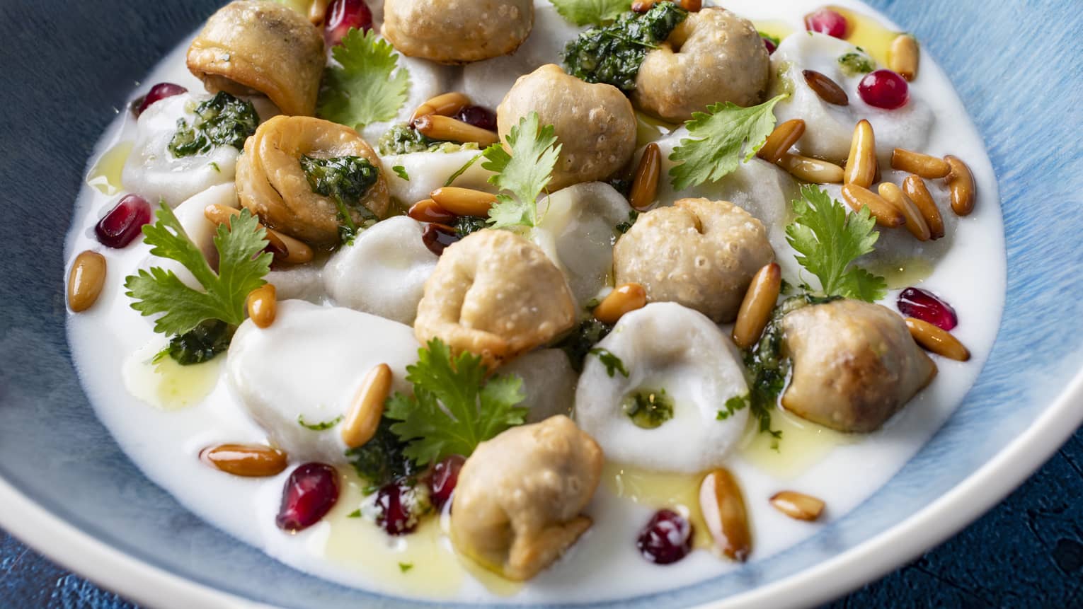 Meat dumplings served with yogurt sauce, garlic, pine nuts, pomegranate and vermicelli rice in a wide blue bowl