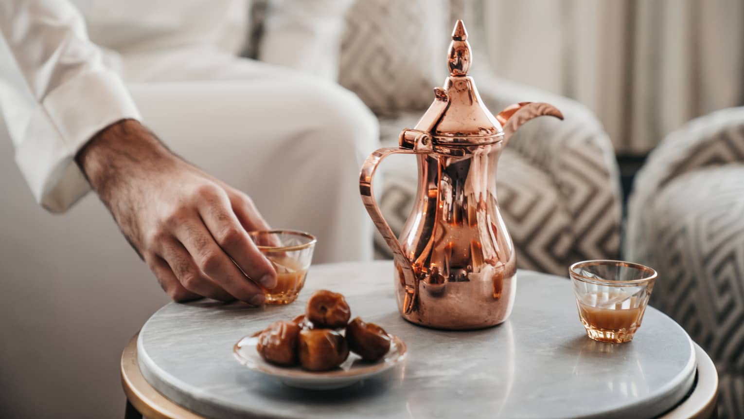 Close up of copper coffee pot, some dried dates on a plate and two small gold-rimmed glasses