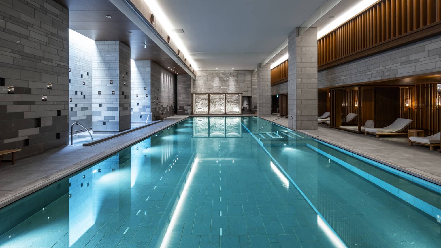 Indoor spa pool flanked by chaise longues and grey brick columns