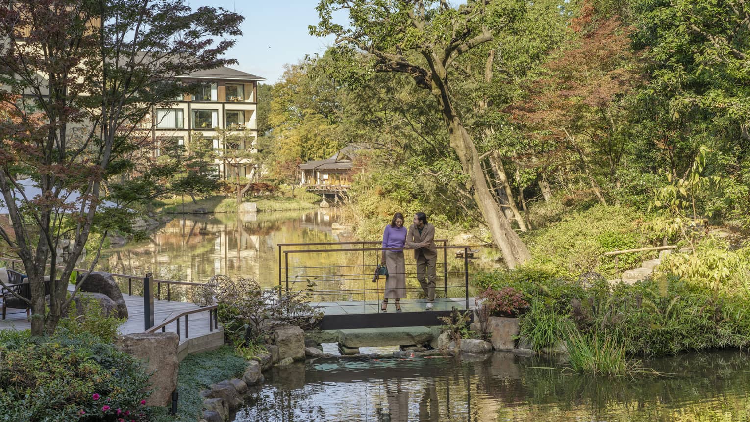 Couple stands on foot bridge overlooking koi pond