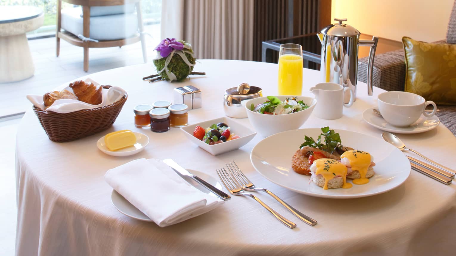 Eggs benedict brunch on plate, fruit and salad in bowls