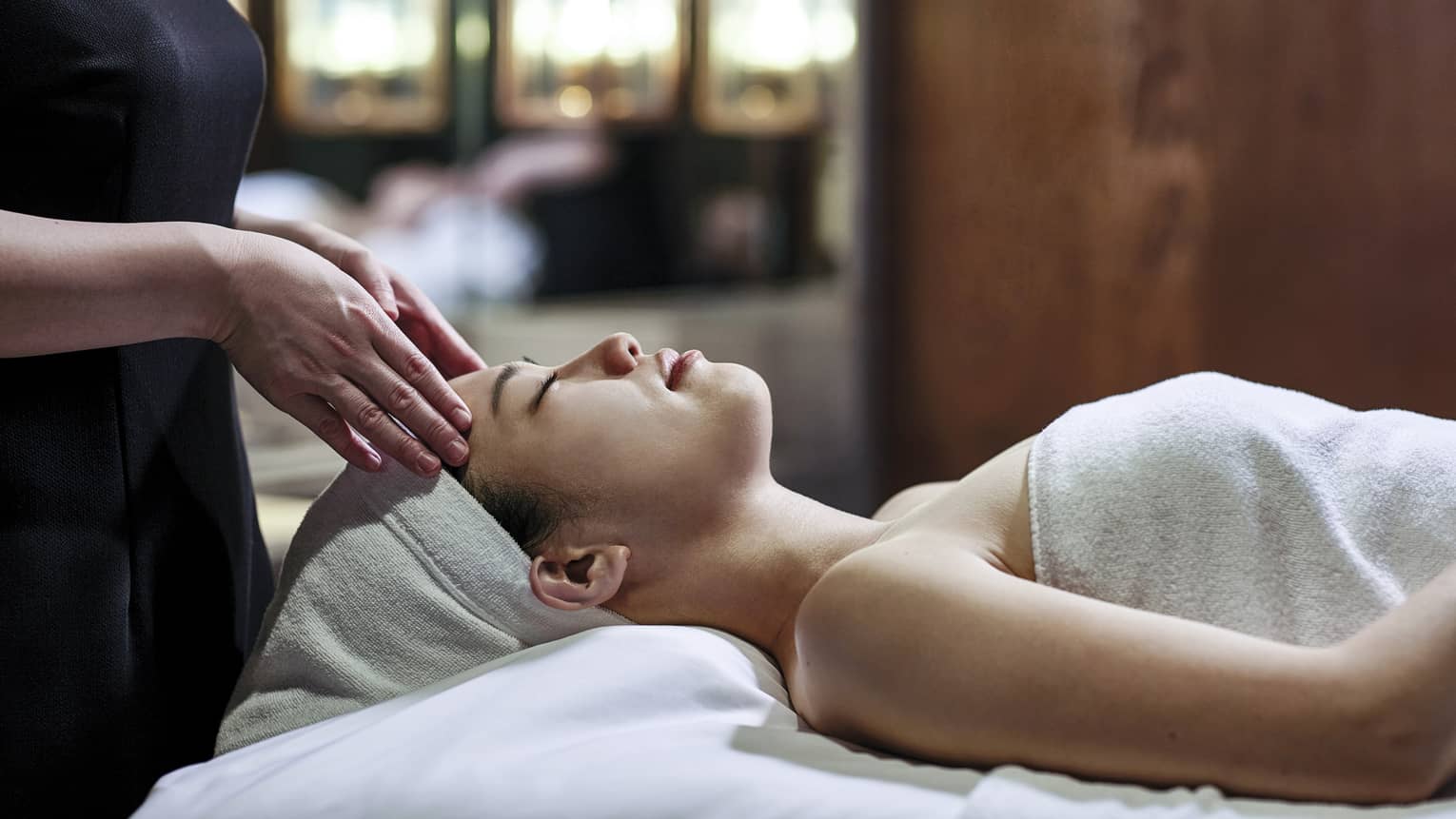 Woman getting a head massage during spa treatment, white towel over her and her head