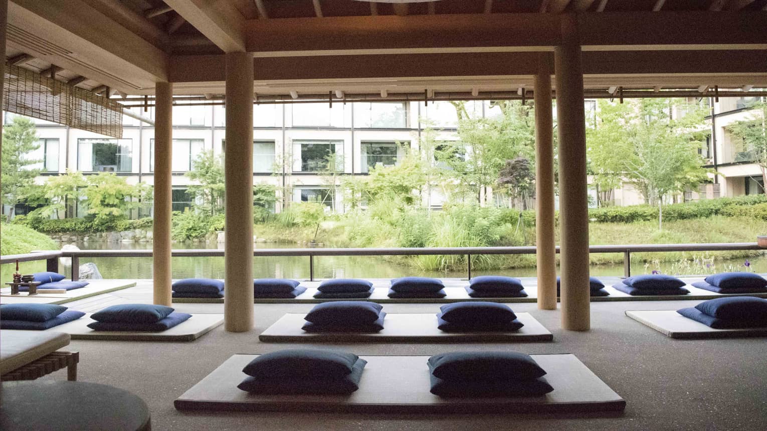 Rows of yoga mats, meditation cushions under pavilion by pond