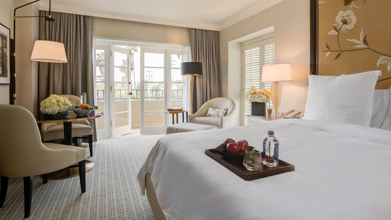 Grand Luxury Suite hotel room bed, wood tray with red apples, water, cafe table by open balcony door