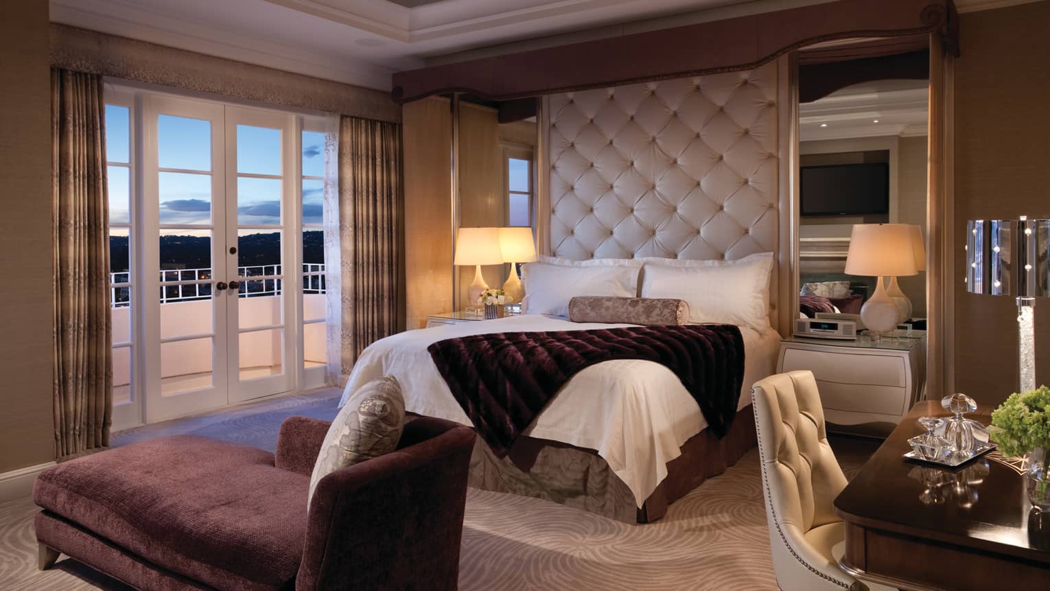 Presidential Suite West purple chaise at foot of hotel bed with tufted headboard, balcony at dusk