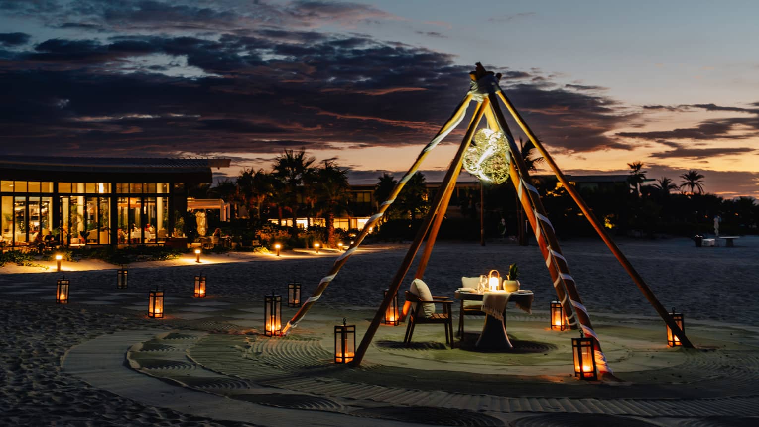 Outdoor tent with a chair and dining table, surrounded by lanterns on the ground in the evening.
