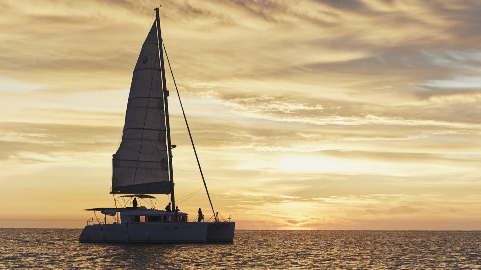 Under a cloudy sky suffused with light at dusk, silhouetted passengers sit aboard a tall sailboat in the the distance. ,Under a cloudy sky suffused with light at dusk, silhouetted passengers sit aboard a tall sailboat in the the distance. . 