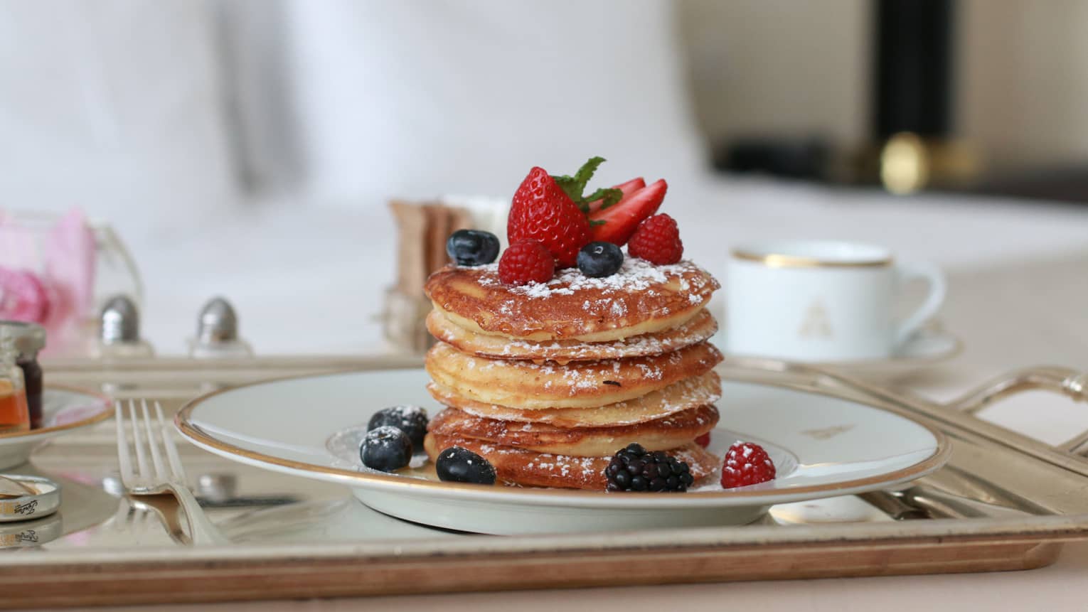 Stack of thick pancakes on plate with dusted icing sugar, fresh berries