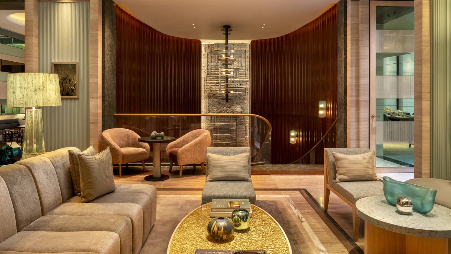 Lounge seating area with beige couch and lounge chairs looking out to staircase with gold bannister