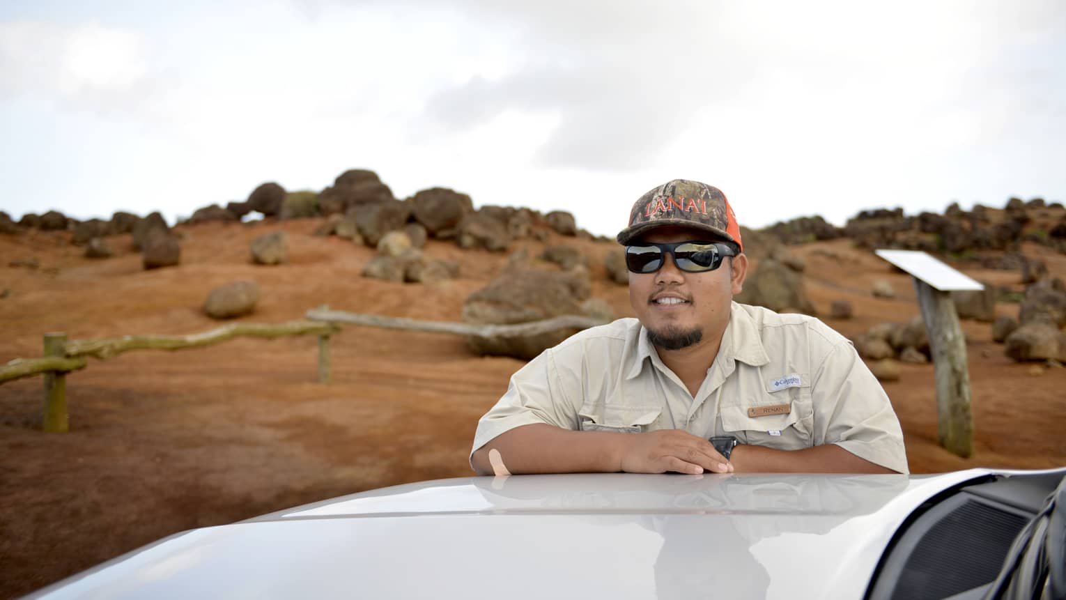 Man leans on top of car, Lanai, Hawaii landscape in the background