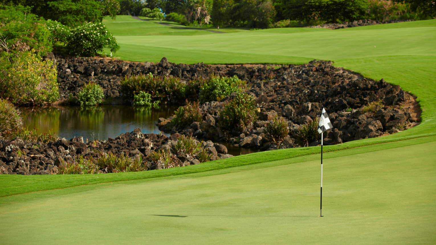 Flag, pole on golf course green near rocks, water 