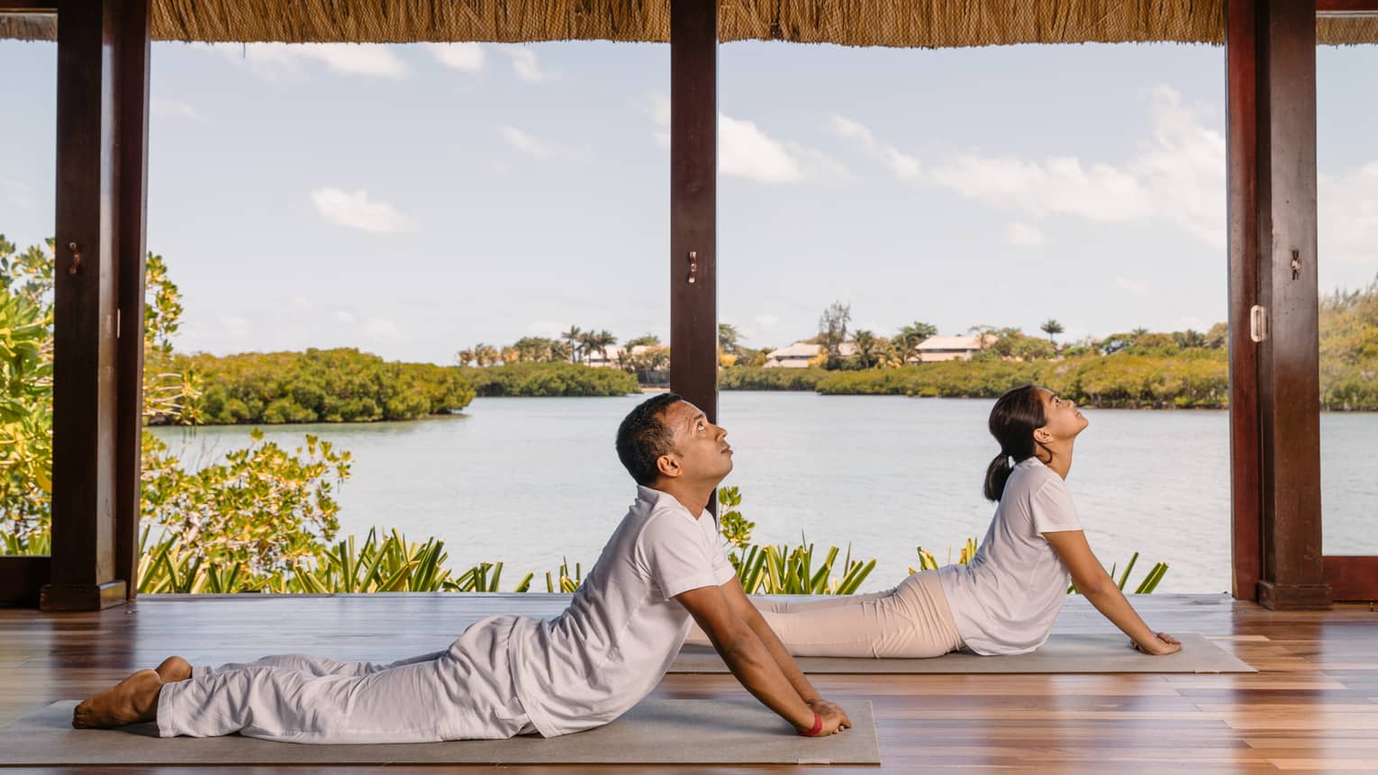 Two people practising yoga in an open to outside area.
