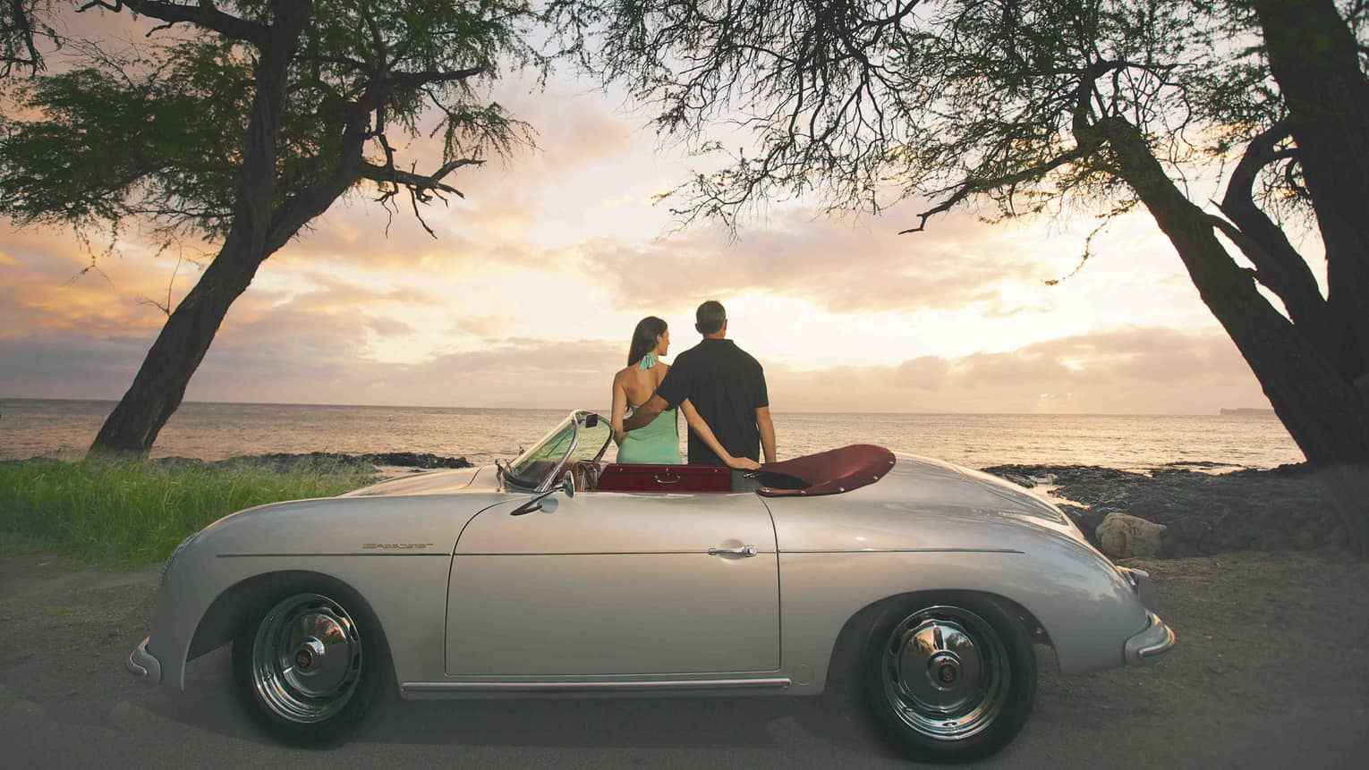 A couple sits on a 1957 Porsche Speedster replica at sunset