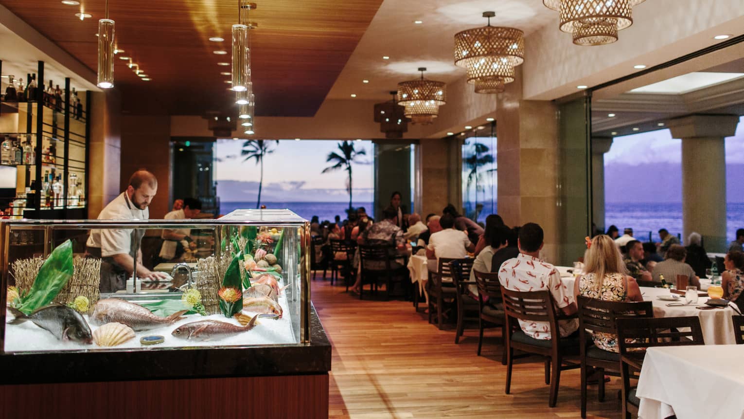 Chef prepares seafood at a sushi bar in a beachfront restaurant during sunset