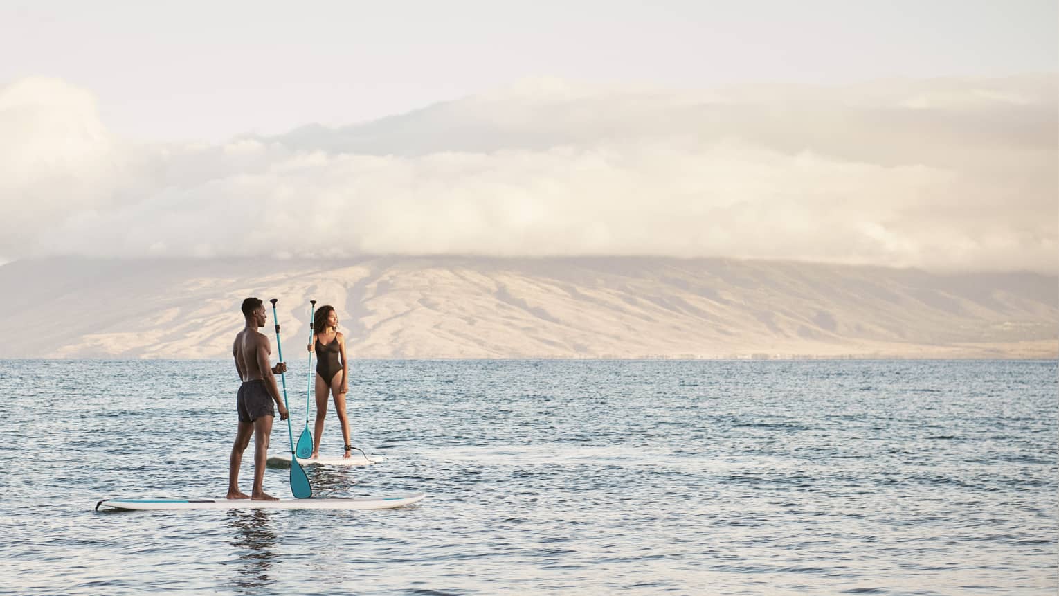 Man and woman stand on SUP paddleboards in the ocean in Maui