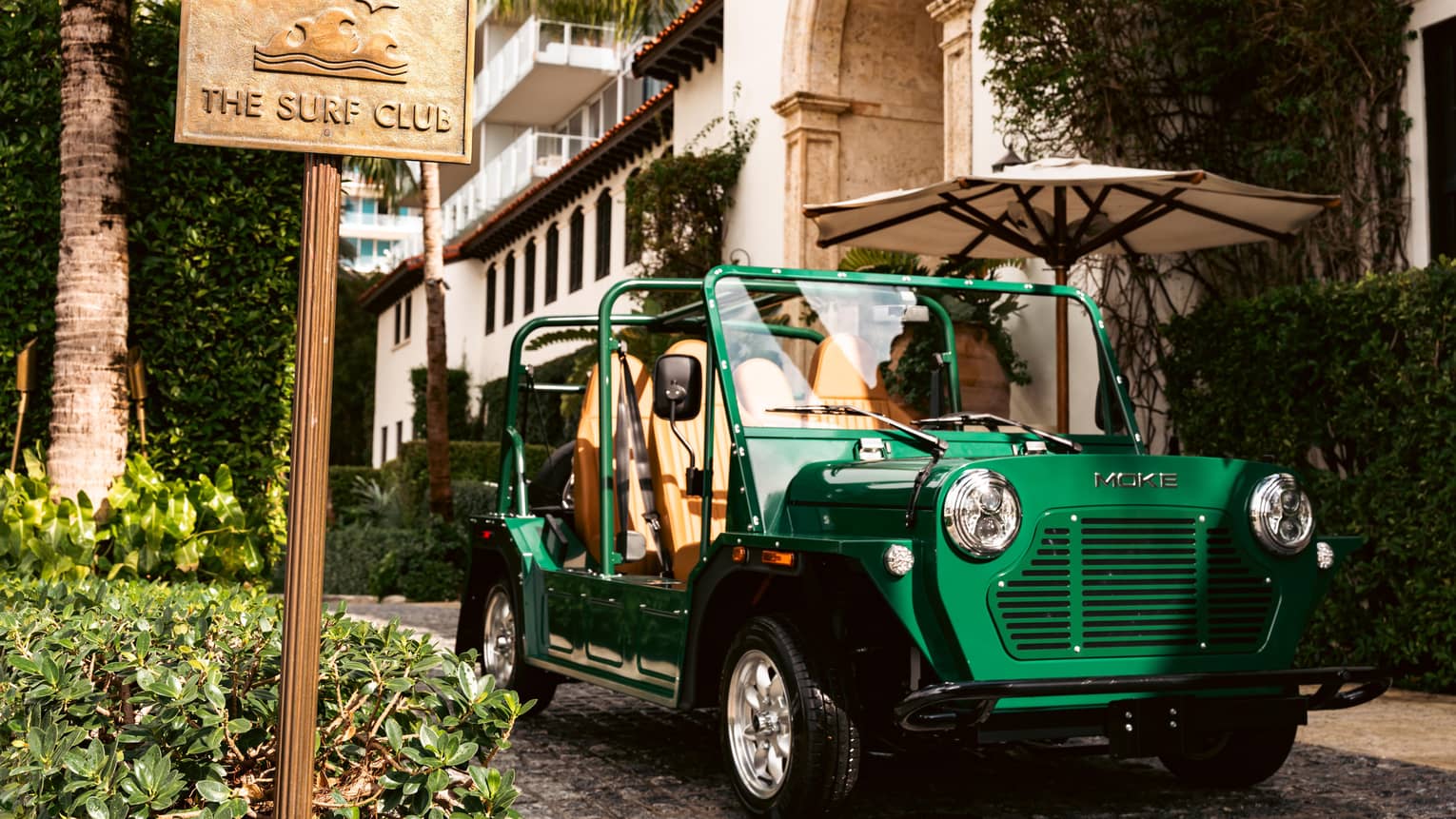 Green MOKE car parked outside of the building next to "The Surf Club" sign.