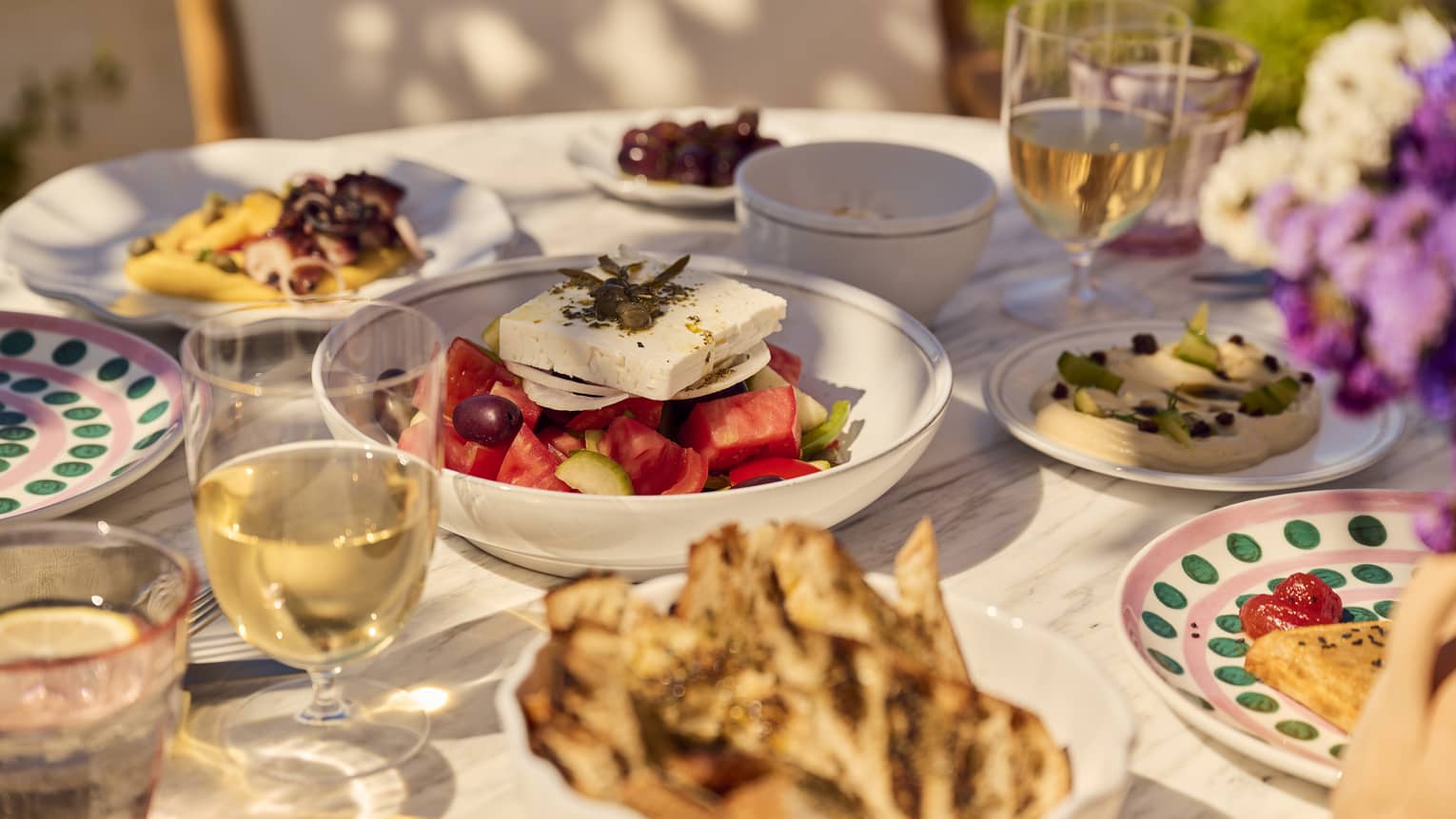An outdoor dining table filled with Greek dishes and glasses of white wine