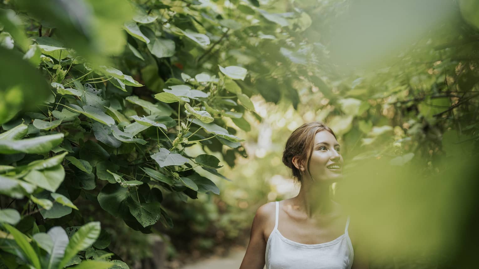 Woman in white tank top walks along heavily tree-lined path