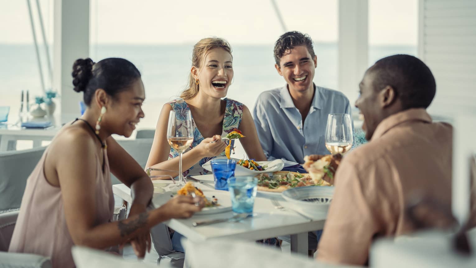 Two couples laugh over a meal at Blu Beach Club