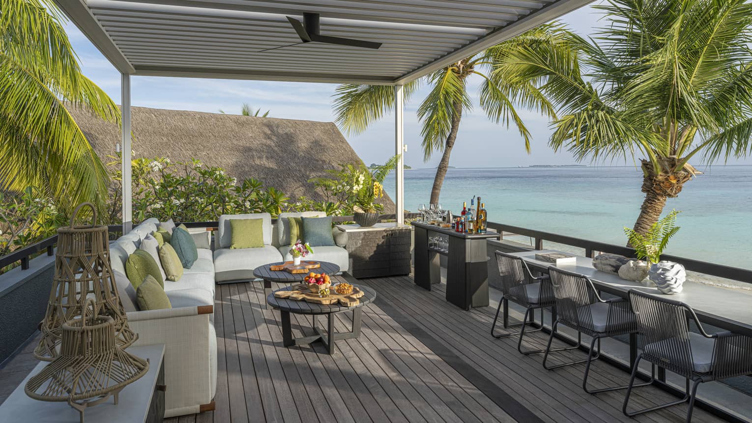 Rooftop terrace of a tropical resort estate, featuring lounge seating and three chairs at a counter ? all overlooking turquoise water