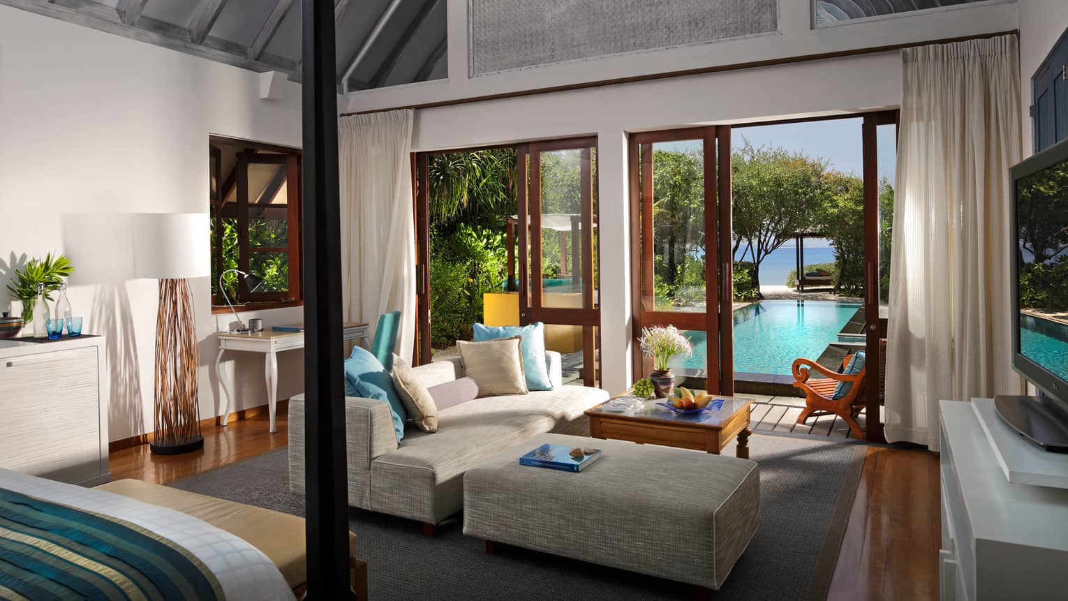 Family Beach Villa with Pool edge of poster bed by sofa, chaise, tables by open doors to patio, pool