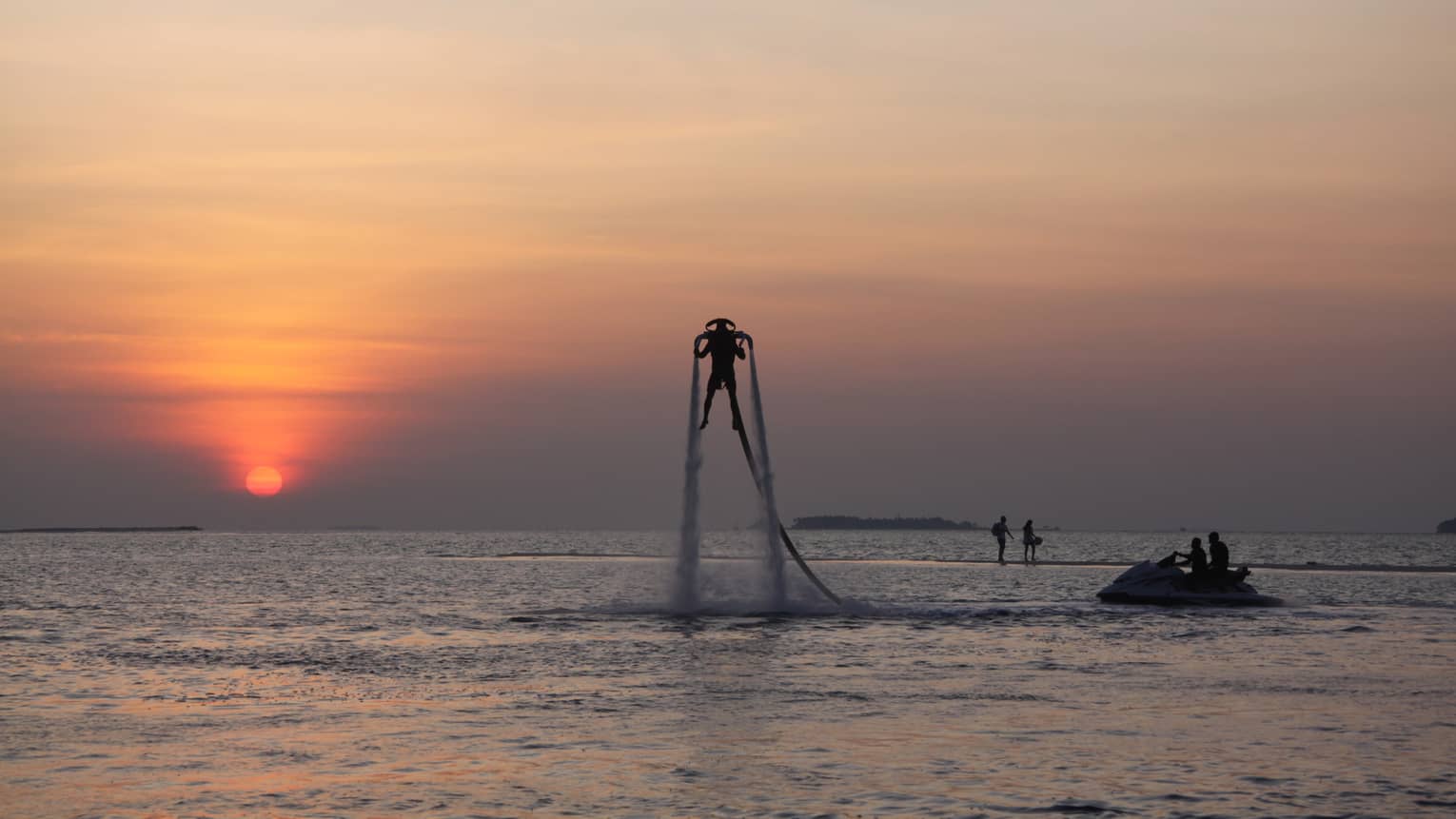 Silhouette of someone with X Jetpack suspended in air over water at sunset