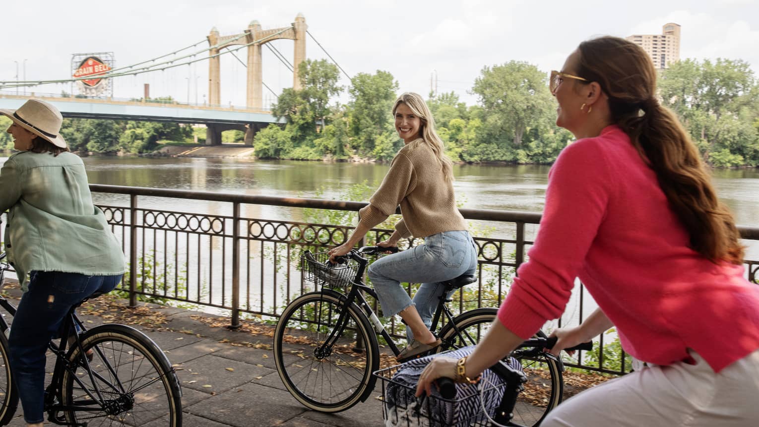 Three guests riding bicycles on the sidewalk near the lake and bridge.