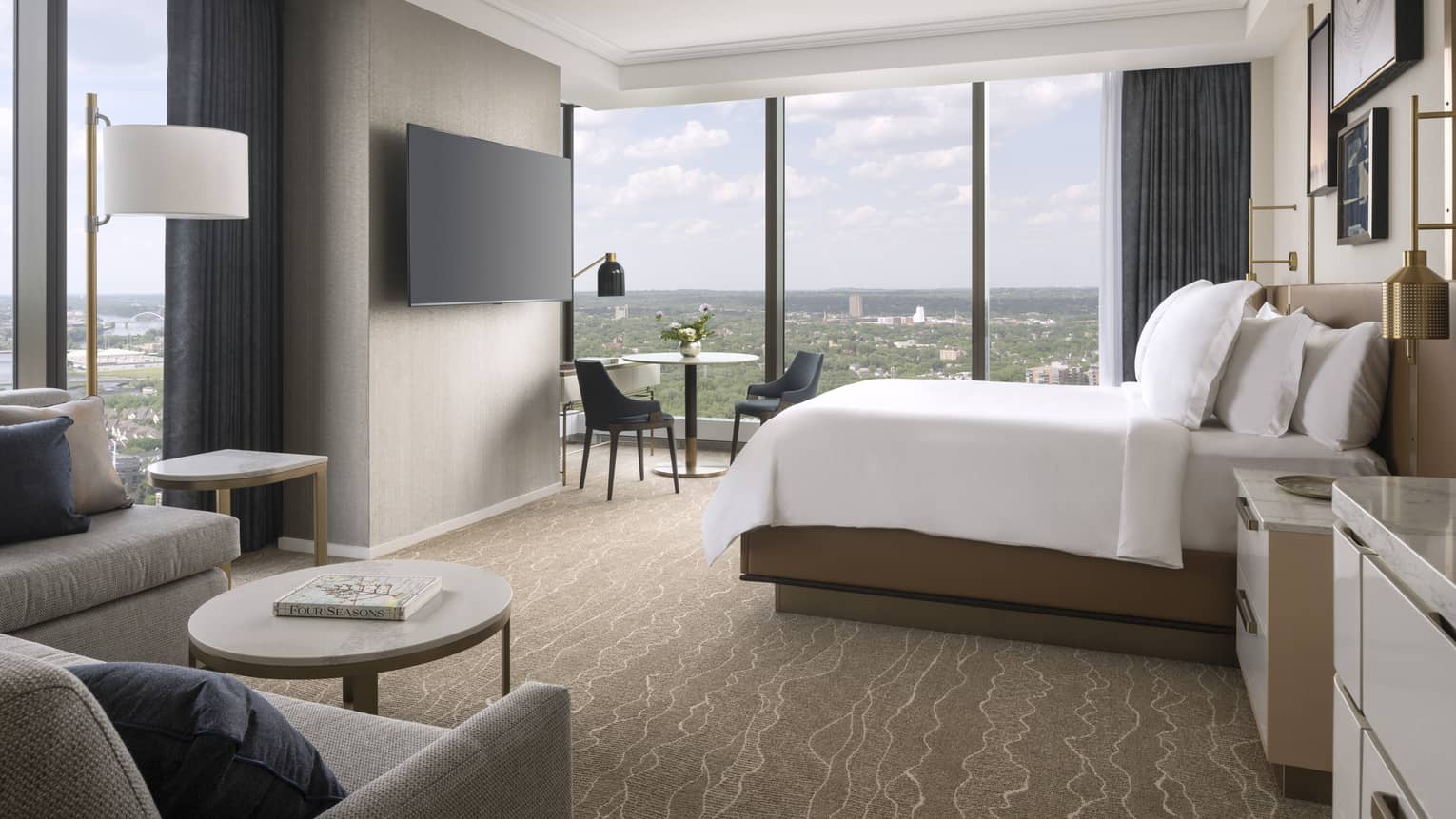Hotel room with king bed, sofa, wall-mounted TV and wall of windows