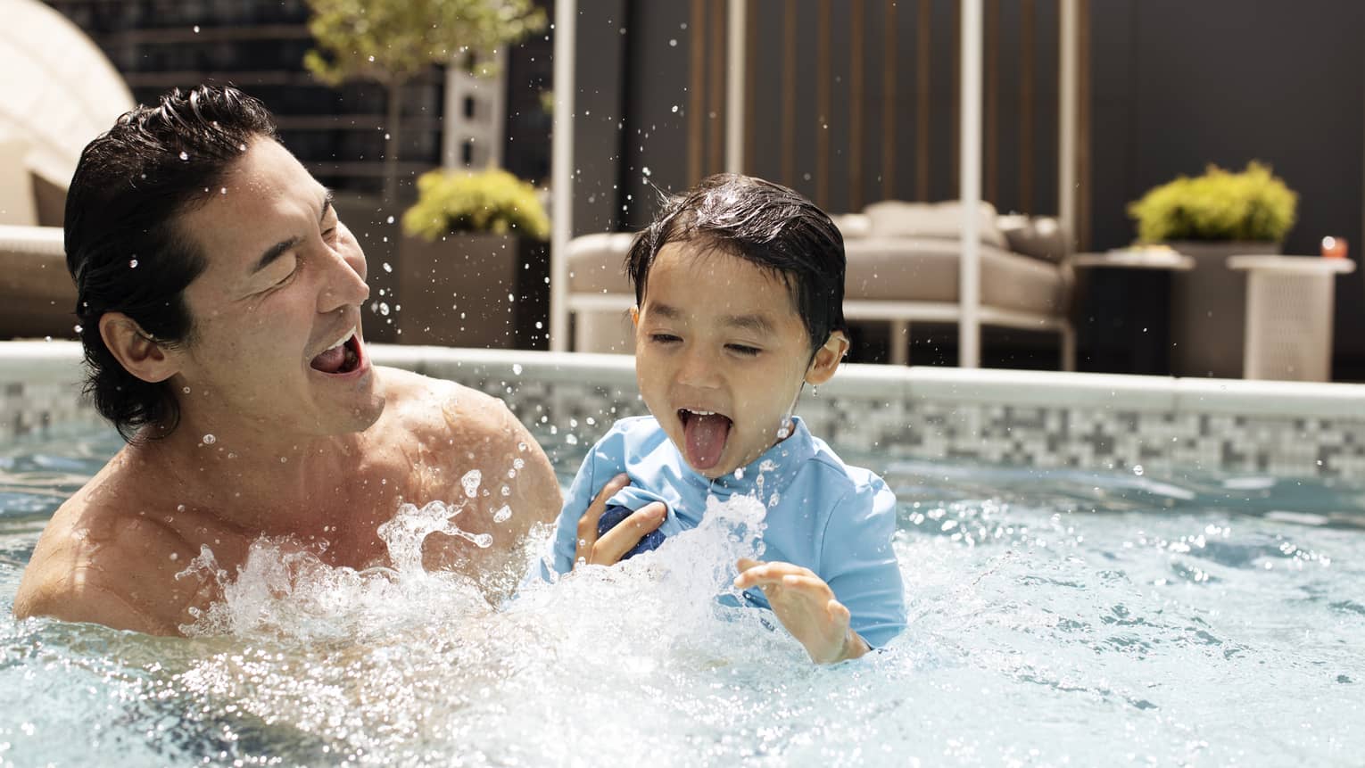 One guest holding a younger guest in the outdoor pool, both laughing.